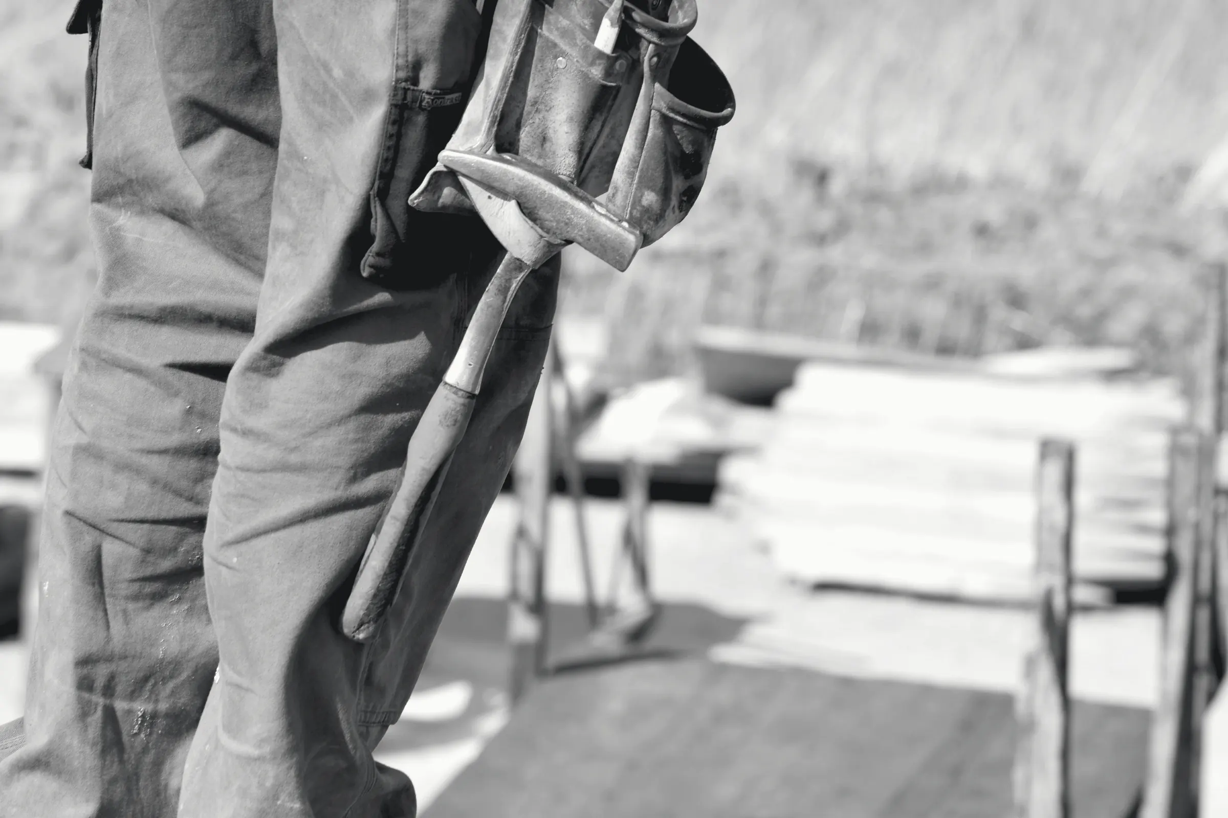 A hammer and pouch on a tool belt, with stacked timber behind